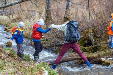 Anne yardım çocuk dağ dere geçmeye hiking. Spor ailesi ile sırt çantaları