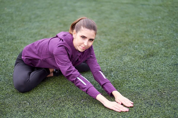 Young sporty woman stretching on a football field