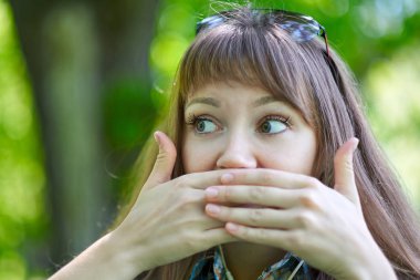Kadın ellerinle ağzını kapatın. Sessizlik jest, dedikodu, gizli. Portre yaz yeşil park