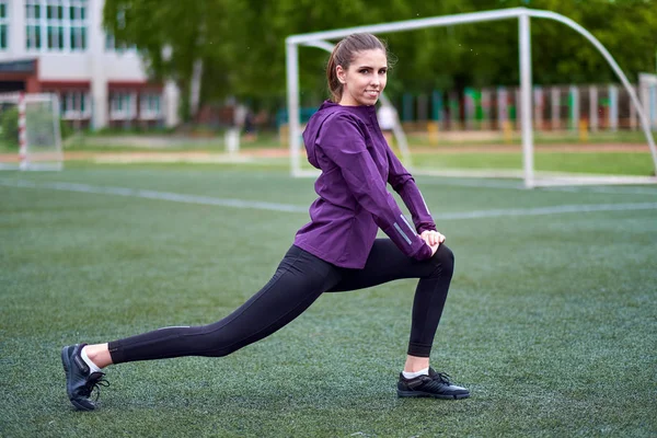 妇女伸展 在足球场上进行健身训练前的年轻女性锻炼 健康的年轻妇女在户外热身 — 图库照片