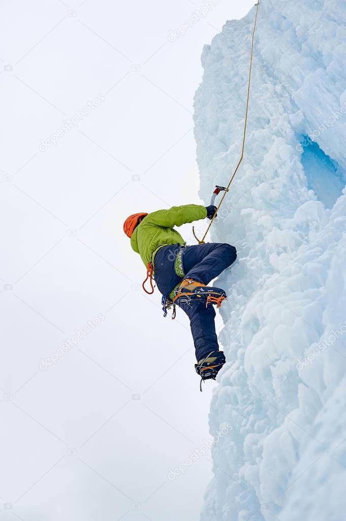 Alpinist man with  ice tools axe in orange helmet climbing a large wall of ice. Outdoor Sports Portrai
