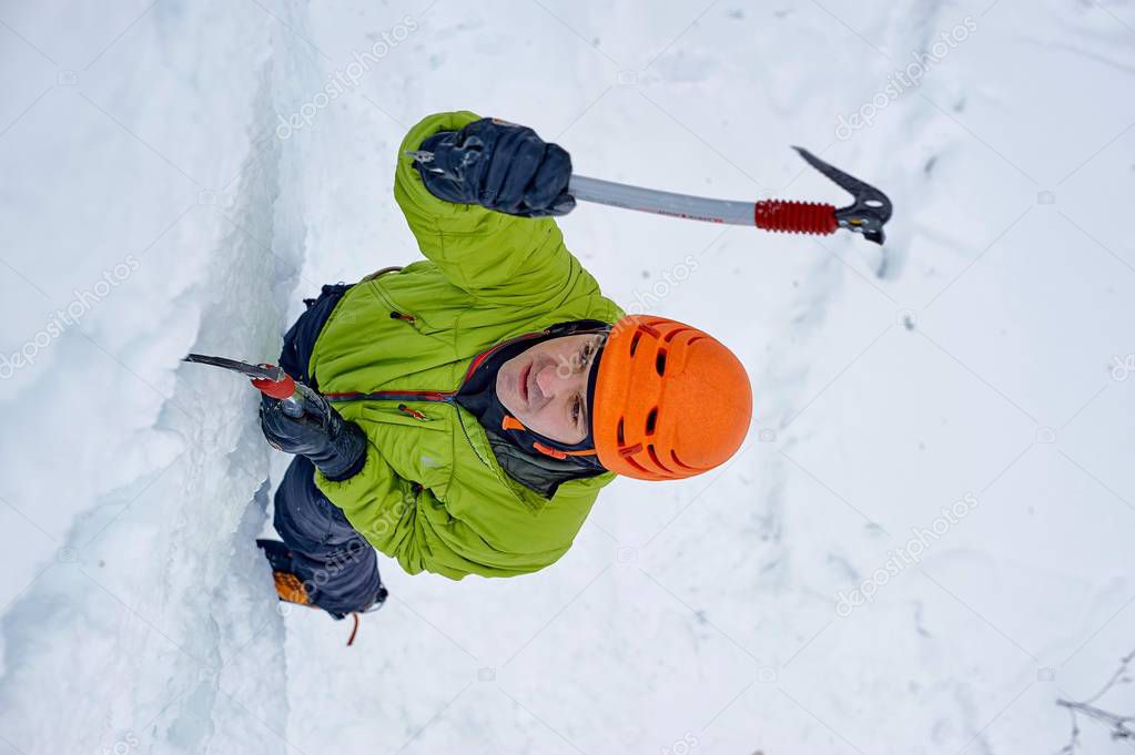 Alpinist man with  ice tools axe in orange helmet climbing a large wall of ice. Outdoor Sports Portrai