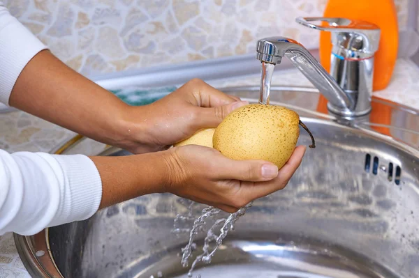 Woman hands washing fruit pears in kitchen under water stream
