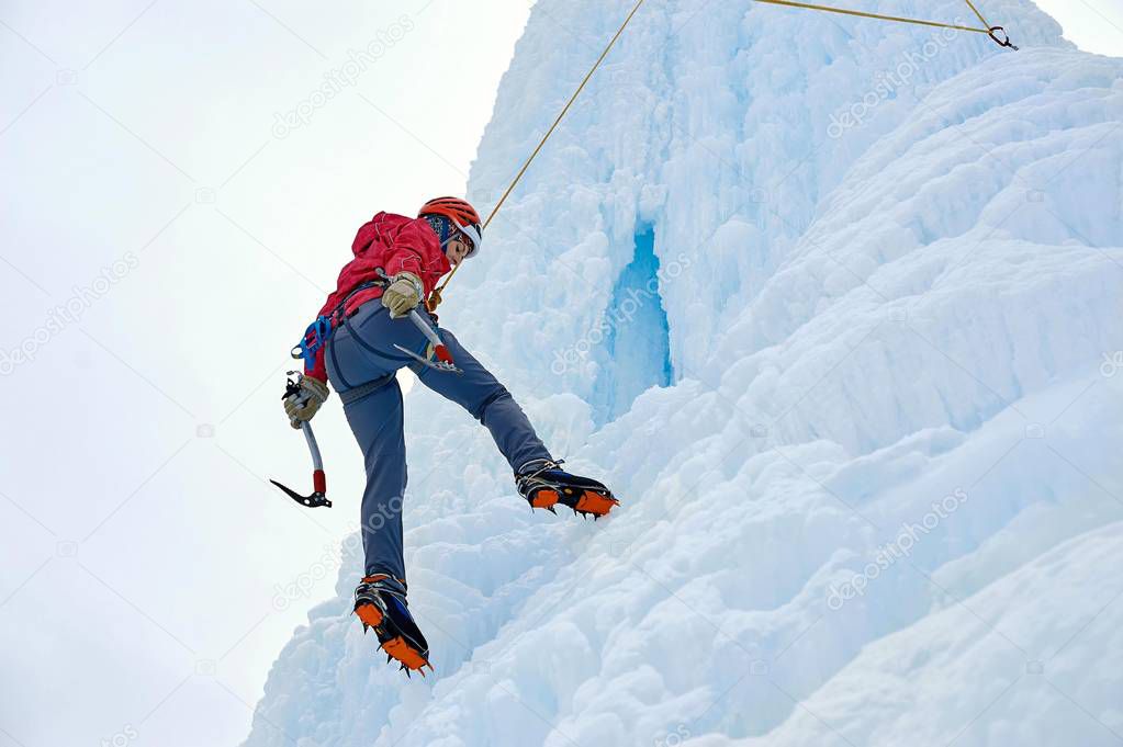 Alpinist woman with  ice tools axe in orange helmet climbing a large wall of ice. Outdoor Sports Portrait