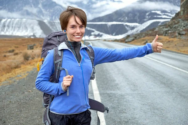 Travel woman hitchhiking. Beautiful young female hitchhiker by the road during vacation trip in mountains