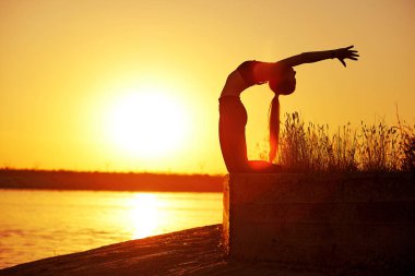 Siluet kadın yoga yapıyor ya da gün batımında ya da gün doğumunda sahilde geriniyor..
