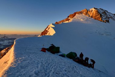 Grup alpinists karlı tepe üzerinde temel kampında yerlerde çadır batımında, Fann, Pamir Alay, Tacikistan