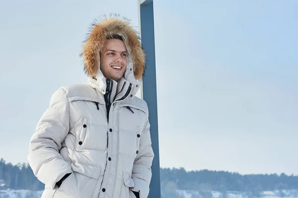 young beautiful man in a white jacket with fur hood in winter Siberia. Fashion portrait .