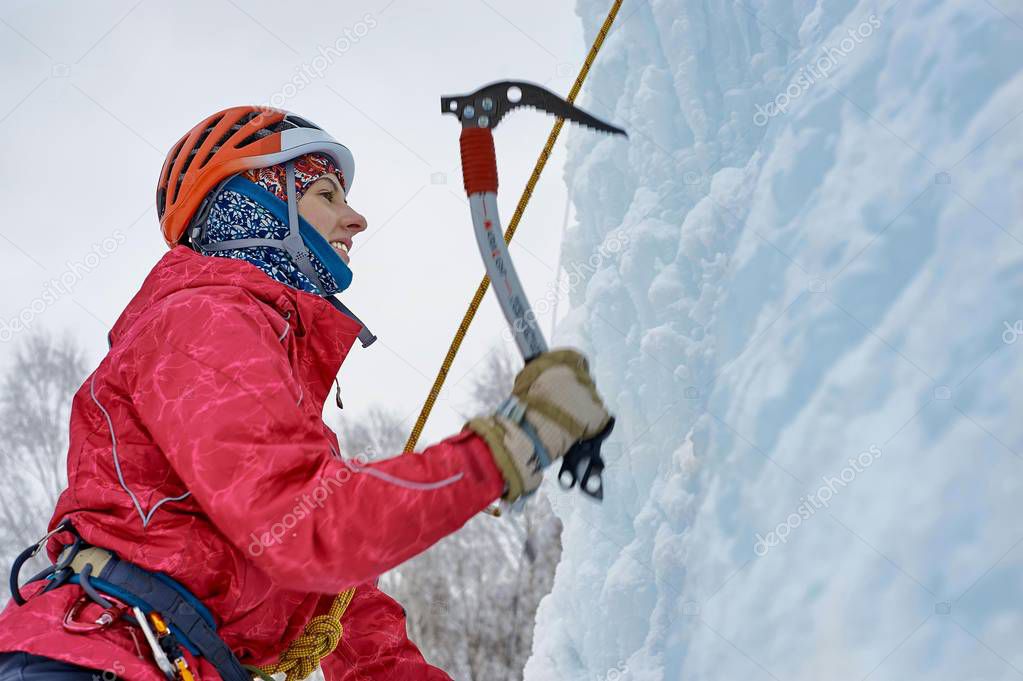 Alpinist woman with  ice tools axe in orange helmet climbing a large wall of ice. Outdoor Sports Portrait