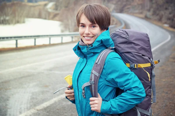 Hiking smiling woman with a backpack in mountains. Beautiful young girl is traveling in the mountains