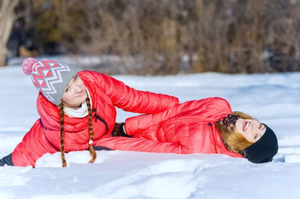 两个年轻的快乐女声躺和拥抱雪地里冬季公园的室外肖像 — 图库照片