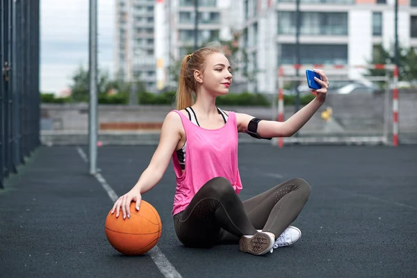 Young woman with basketball using phone after training, making selfie.