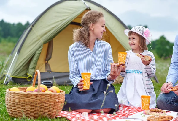 Happy family on picnic at camping. Mother and daughter eating near a tent in meadow or park — Stock Photo, Image
