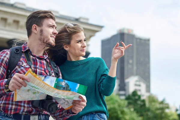 Young couple with a map in the city. Happy tourists sightseeing city with map — Stock Photo, Image