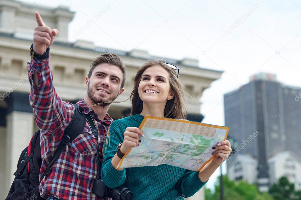 Young couple with a map in the city. Happy tourists sightseeing city with map