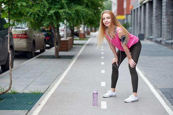 Jovem mulher descansando depois de correr em uma pista da cidade com uma garrafa de água — Fotografia de Stock