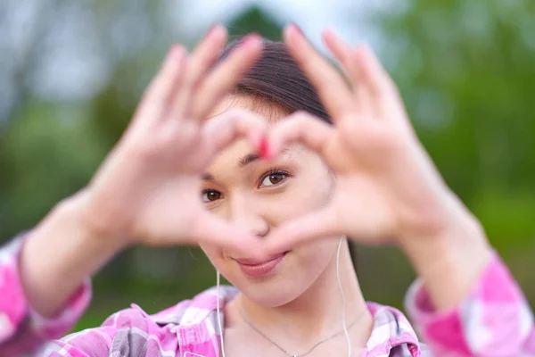 Schöne asiatische Frau, die durch Herzgeste mit den Händen im sommergrünen Park schaut — Stockfoto