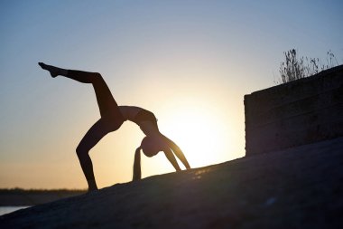 Siluet kadın yoga yapıyor ya da gün batımında ya da gün doğumunda sahilde geriniyor.