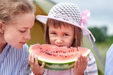 Anne ve kızı karpuz yeme bir çadırda çayır veya park yakınındaki. Mutlu aile piknik kamp, Tarih.