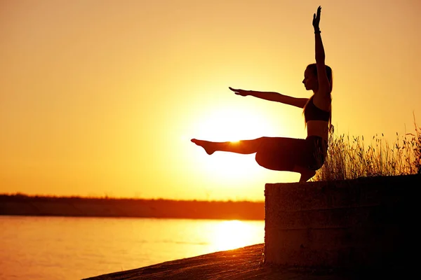 Siluet kadın yoga yapıyor ya da gün batımında ya da gün doğumunda sahilde geriniyor. — Stok fotoğraf