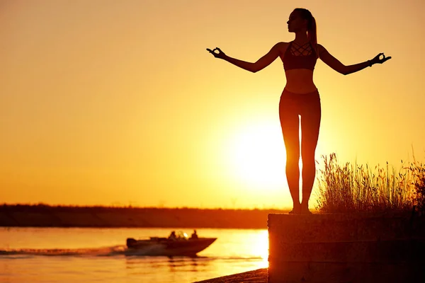 Gün batımında veya gün doğumunda sahil iskelesinde yoga duruşu ile siluet kadın — Stok fotoğraf