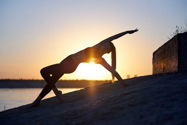 Siluet kadın yoga yapıyor ya da gün batımında ya da gün doğumunda sahilde geriniyor. — Stok fotoğraf