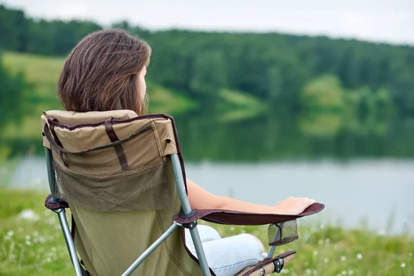若い女性のフリーランサーは椅子に座って湖の近くで自然の中でリラックスしています。夏の野外活動。国立公園での冒険旅行。レジャー休暇リラックス — ストック写真