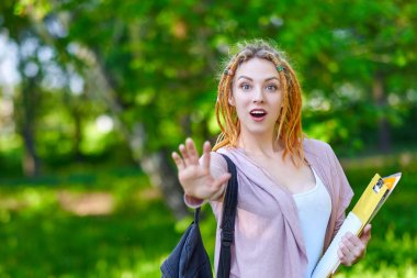 Durdurmak. Klasörler ve sırt çantası ile Kadın Öğrenci yeşil yaz parkı el sallayarak