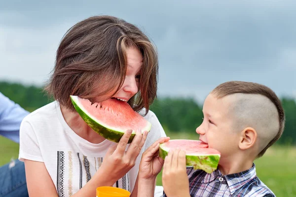 Anne ve oğlu çayırda veya parkta karpuz yiyor. Mutlu bir aile piknikte. açık hava portresi Küçük çocuk ve anne — Stok fotoğraf
