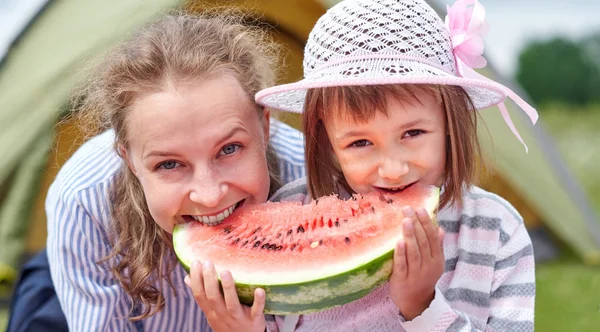 Madre e figlia mangiare anguria vicino a una tenda nel prato o parco. Famiglia felice al picnic in campeggio . — Foto Stock