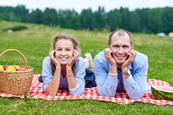 Young couple in love on picnic lying on tablecloth in red cell. Love couple resting in nature in meadow or park — Stock Photo, Image