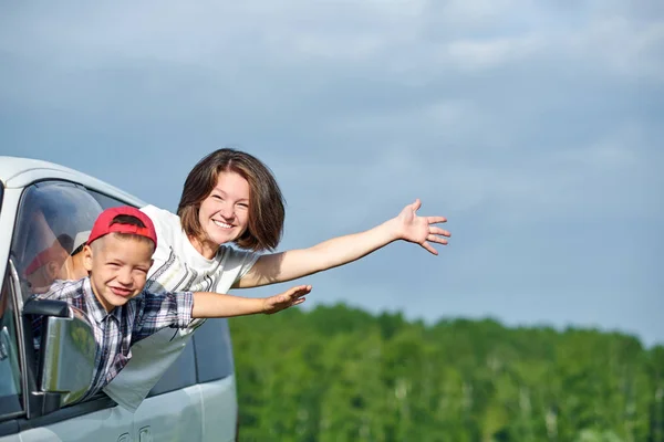 Mutlu genç kadın ve çocuğu pencereden dışarı bakıyor. Aile arabayla seyahat ediyor. — Stok fotoğraf
