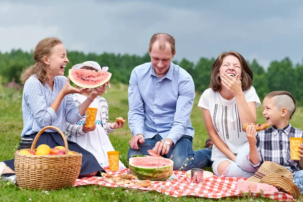 Mutlu aile piknikte karpuz yiyor. Çayır ya da parkta piknik. Genç arkadaşlar ve onların çocukları doğada — Stok fotoğraf