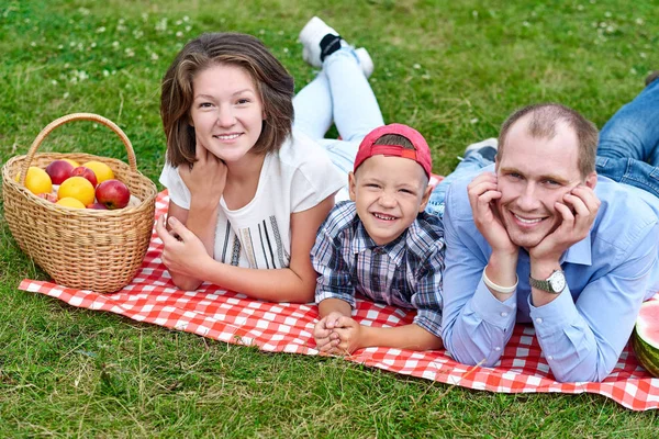 Mutlu bir aile doğada dinleniyor. Anne, baba ve çocuk çayırda kareli ekose üzerinde eğleniyor ve uzanıyor. — Stok fotoğraf