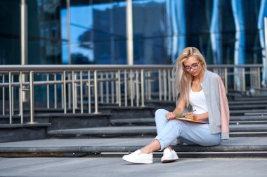 Şehir caddesinde merdivenlerde oturan çekici mutlu bir kadının portresi