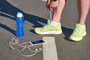 koşucu kadın koşu ayakkabıları bağcıklar su şişesi ve akıllı telefon ve kulaklık ile koşmak parça stadyumda yarış için hazırlanıyor