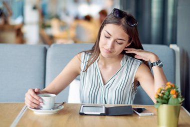 Kafede kitap okuyan ve kahve içen genç bir iş kadını.