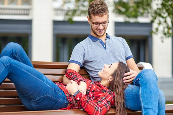Bellissimo ritratto di una giovane coppia. Sono seduti sulla panchina, abbracciati e baciati. — Foto Stock