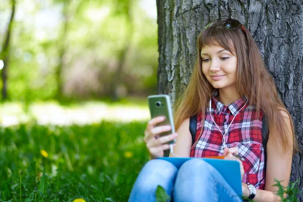 Güneşli bir dayteenager üzerinde bir bankta bir parkta otururken, on-line Alışveriş kavramı bir akıllı telefon ile güzel neşeli kız