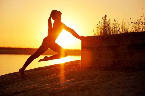 Siluet kadın yoga yapıyor ya da gün batımında ya da gün doğumunda sahilde geriniyor. — Stok fotoğraf