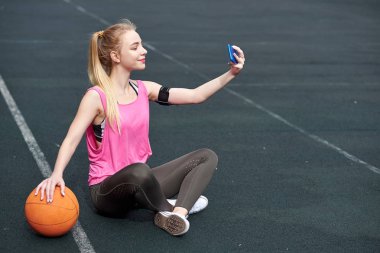 Basketbol antrenmanından sonra telefon kullanan, selfie çeken genç bir kadın.