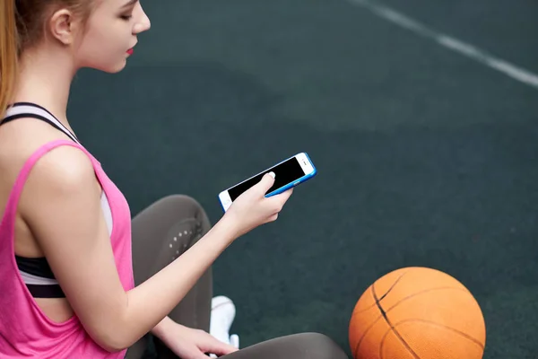 Mujer joven con baloncesto usando el teléfono después del entrenamiento. Pantalla negra — Foto de Stock