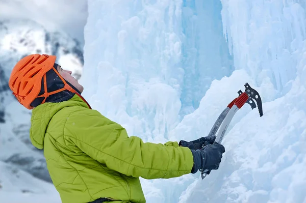 Uomo alpinista con piccozza in casco arancione arrampicata su una grande parete di ghiaccio. Ritratto sportivo all'aperto. — Foto Stock