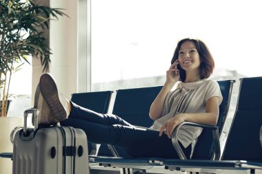 Sıradan bir genç kızın el bagajıyla oturduğu hava yolculuğu konsepti. Havaalanındaki kadın terminalde bekliyor.