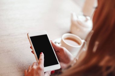 Akıllı telefonları, kulaklıkları ve bir fincan çayı olan kadın elleri. Grafik görüntüleme montajı için