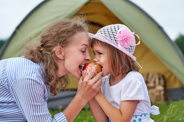 母親と娘は牧草地や公園のテントの近くでリンゴを食べる キャンプでのピクニックの幸せな家族 — ストック写真