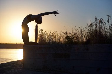 Siluet kadın yoga yapıyor ya da gün batımında ya da gün doğumunda sahilde geriniyor..