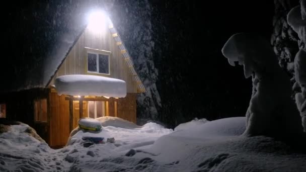 Hegyi ház és lucfenyő hóban éjszaka az erdőben. Havazik. — Stock videók