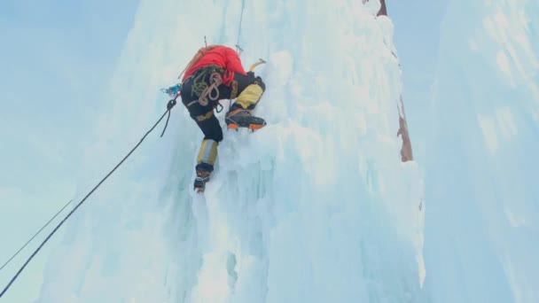 Альпинист с топором для льда, взбирающийся на большую ледяную стену. — стоковое видео
