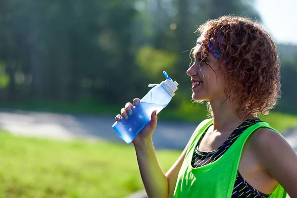 La coureuse fait une pause, boit de l'eau pendant la course dans le parc d'été — Photo